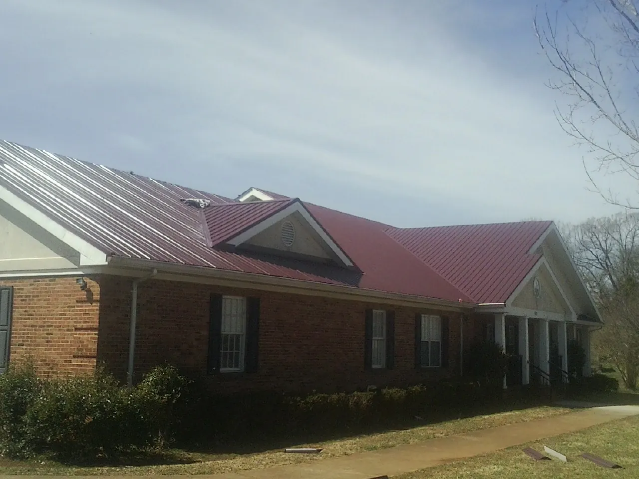 Red metal roof with gabled entries on a long brick building, from a Hail Damage Roof Repair job in Lone Tree
