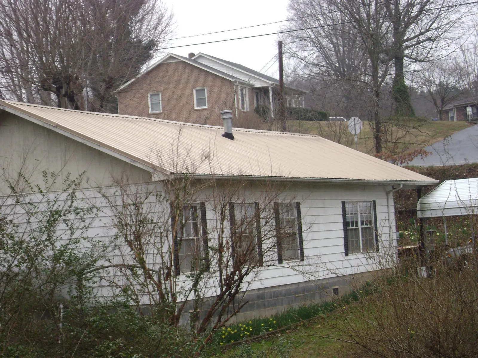 Tan metal roof on a white sided house set into a hillside — Commercial Roofing by Roofing Brothers in Lone Tree