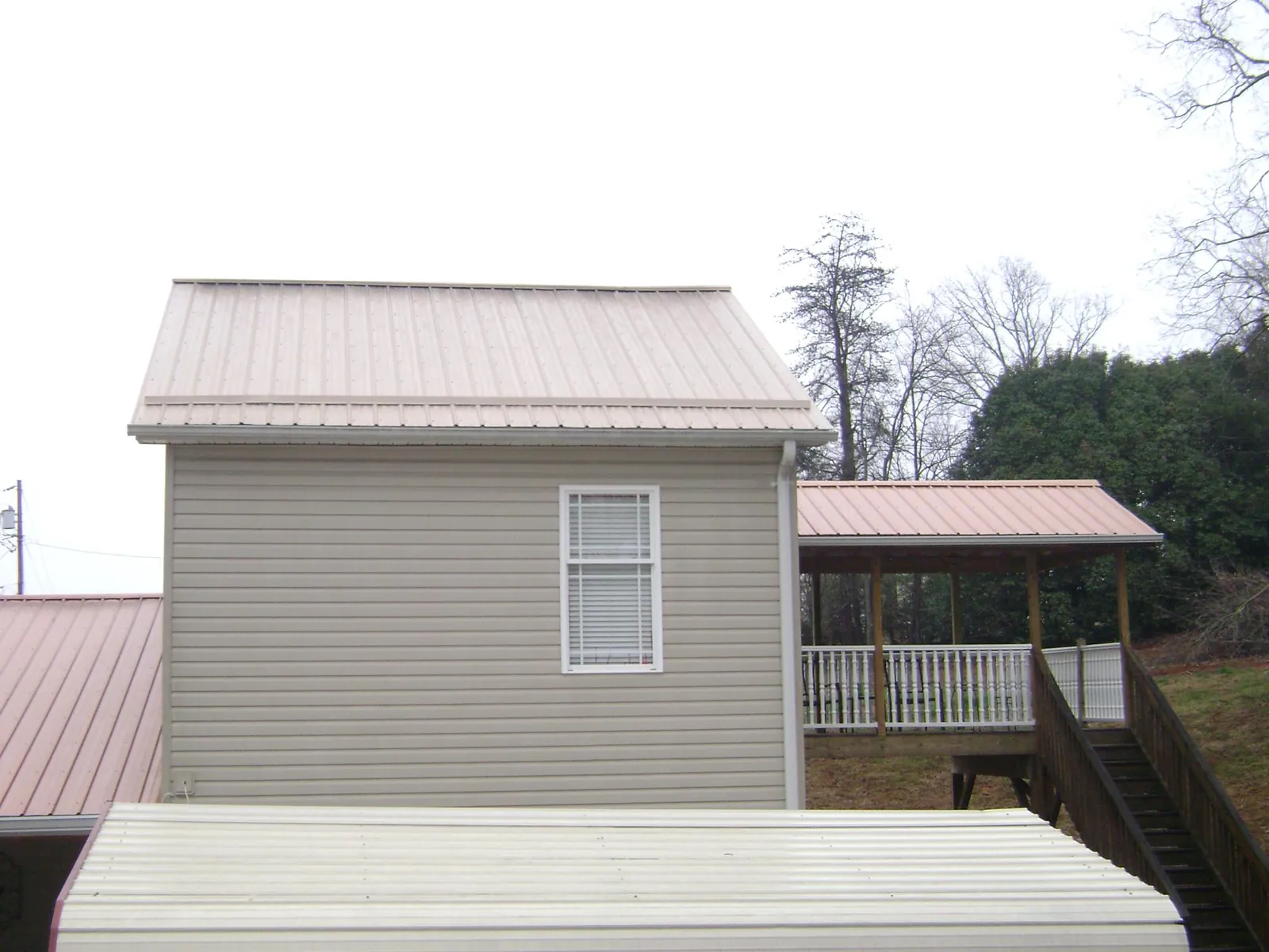 Tan metal roofs on a two story addition and attached porch, from a Roof Replacement job in Lone Tree